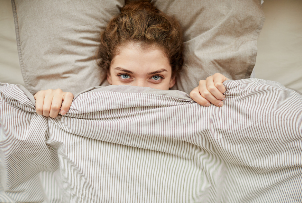 woman laying down pulling a blanket over half her face