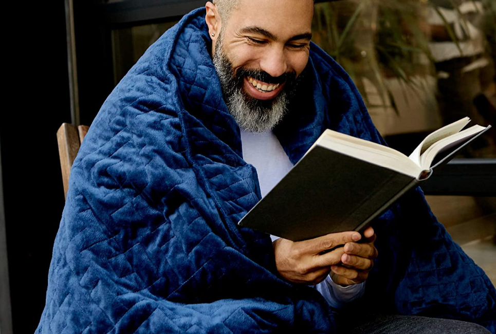 mean wrapped up in blue weighted blanket smiling and reading book