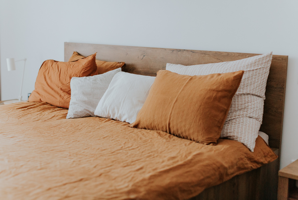 trendy bed made with orange sheets and throw pillows