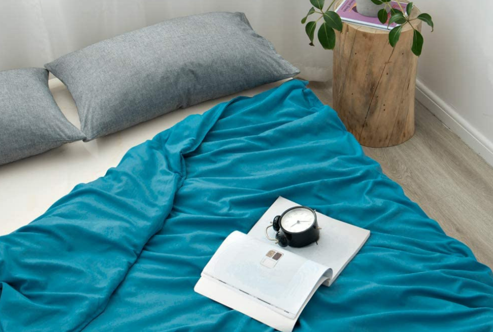 open book and alarm clock resting on teal blanket on bed