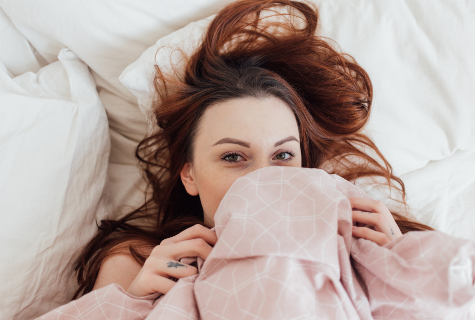 woman laying in bed pulling pink sheets up to face
