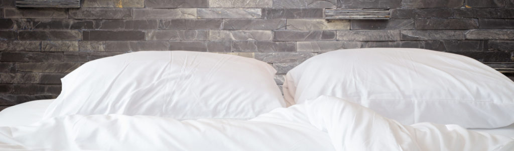 White Bedding Sheets and Pillow on Natural Stone Wall Room
