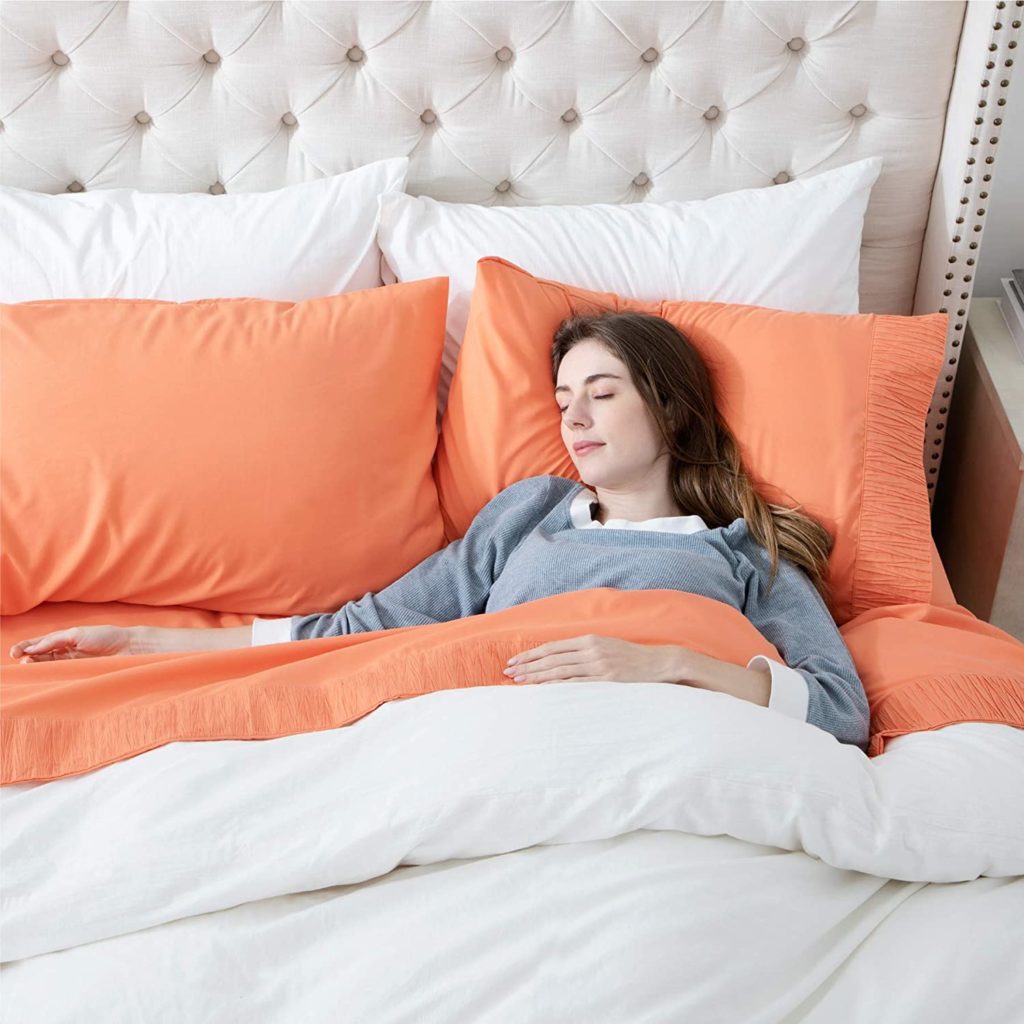 woman sleeping peacefully in bed with orange sheets and a white comforter