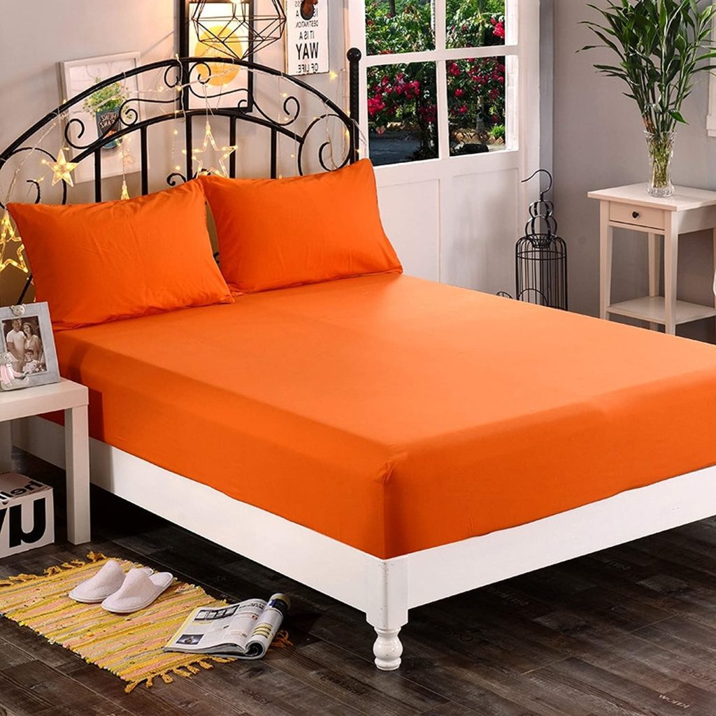 bed made with orange sheets and twinkle lights on headboard