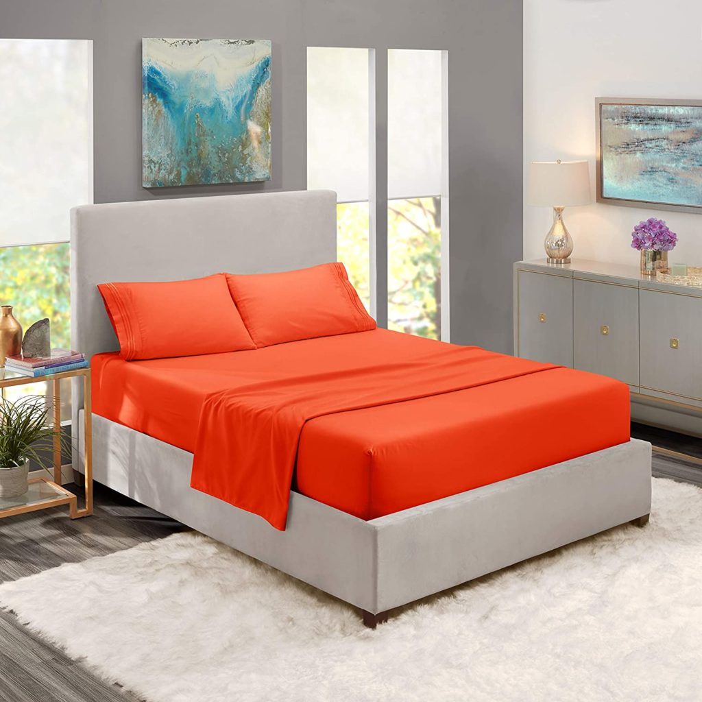 neatly made bed in trendy room with orange sheets