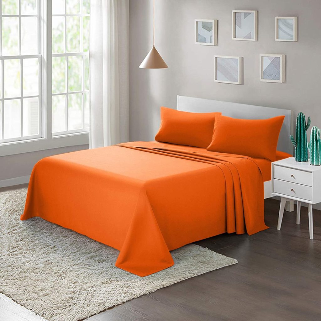 neatly made bed in modern room with orange sheets