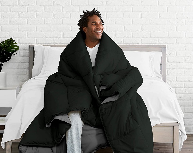 Man wrapped up in black oversized comforter sitting on bed