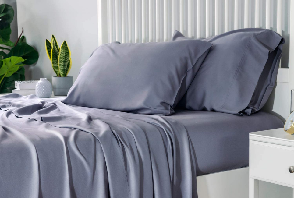 grey sheets on bed in clean room with faux plants