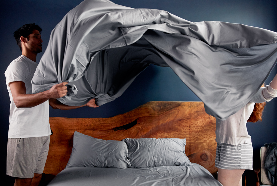 couple making bed with grey sheets