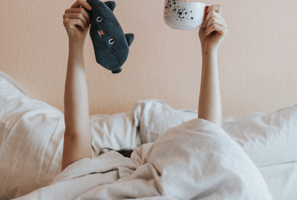 persons arm raising up in bed holding coffee mug and cat sleeping mask