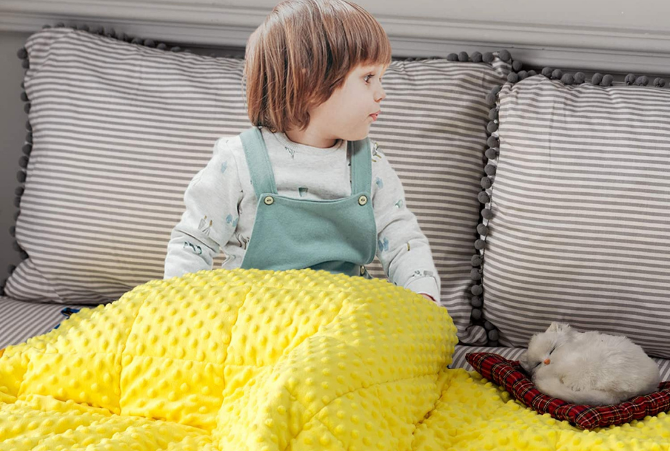 young child sitting on bed with yellow blanket over his lap