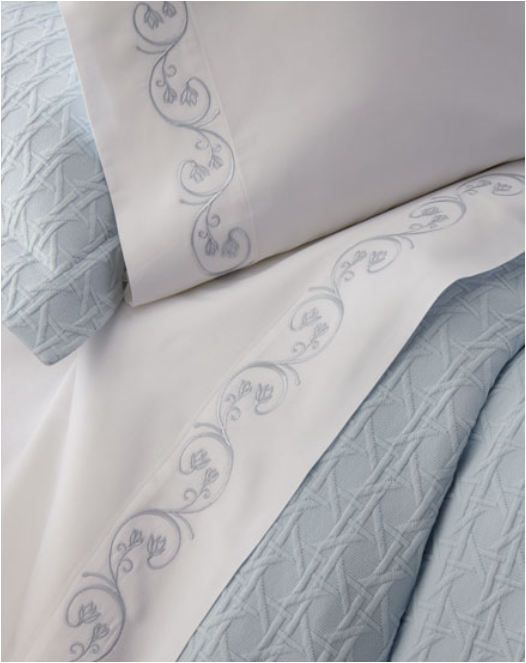 Blue textrued comforter and white sheets on bed with blue embroidery