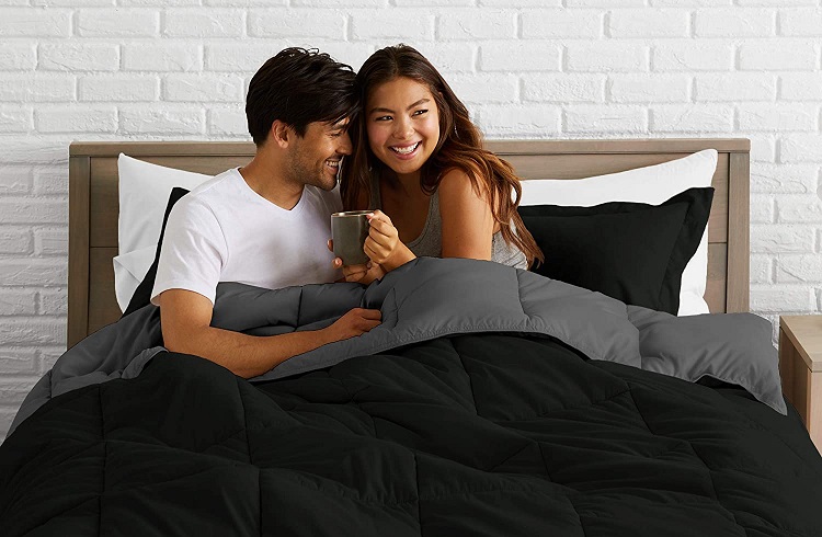 Happy couple giggling sitting up in bed under a black and grey comforter
