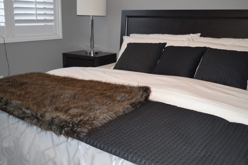 bed made with neutral bedding and fux throw blanket