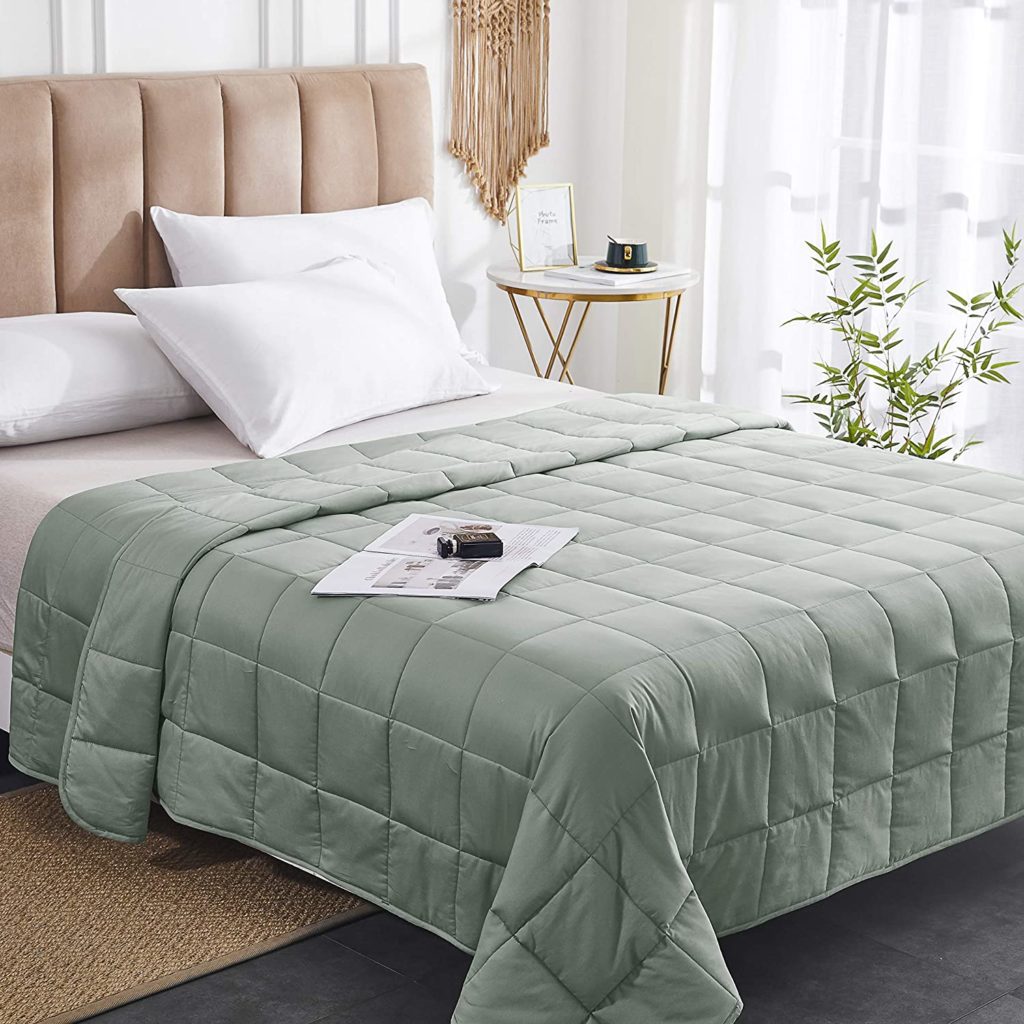 bed neatly made in room with sage green weighted blanket and magazine on bed