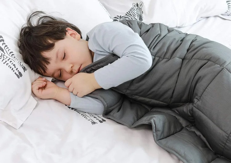 child sleeping peacefully under grey weighted blanket