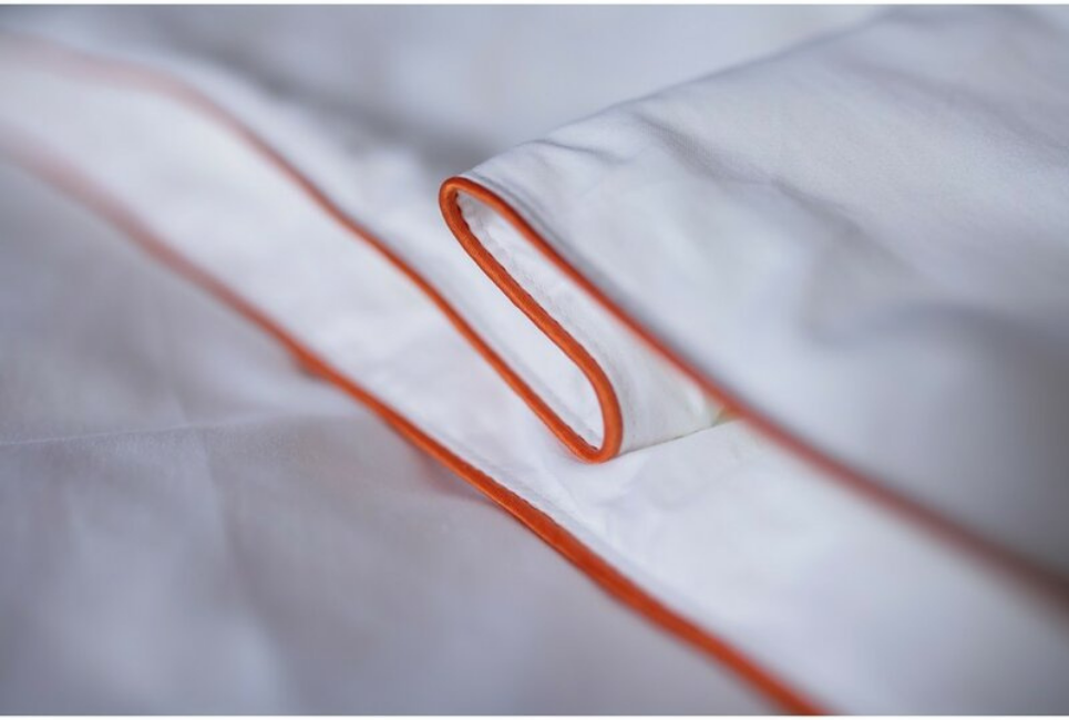 close up of white silk comforter with orange piping trim