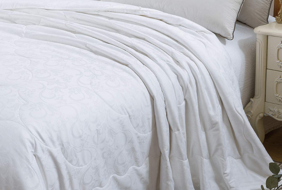 corner of all white patterned silk comforter on bed