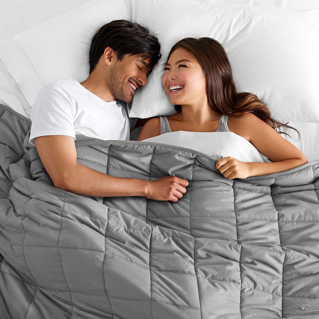 couple laughing in bed under grey weighted blanket