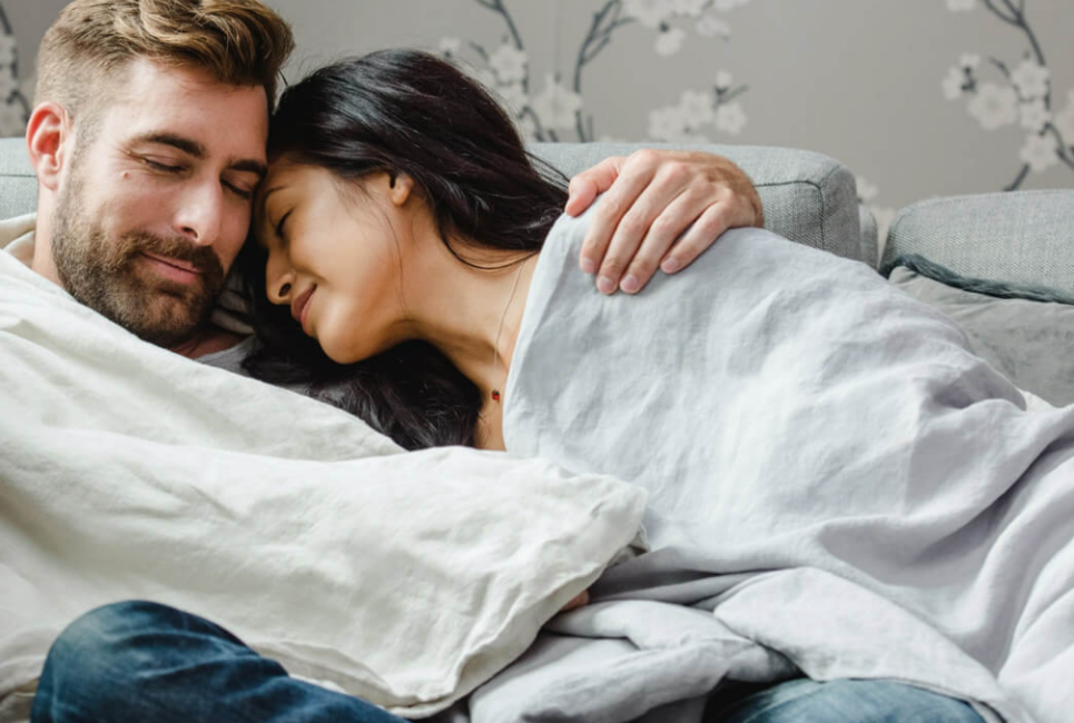 couple snuggling on couch under beige blanket