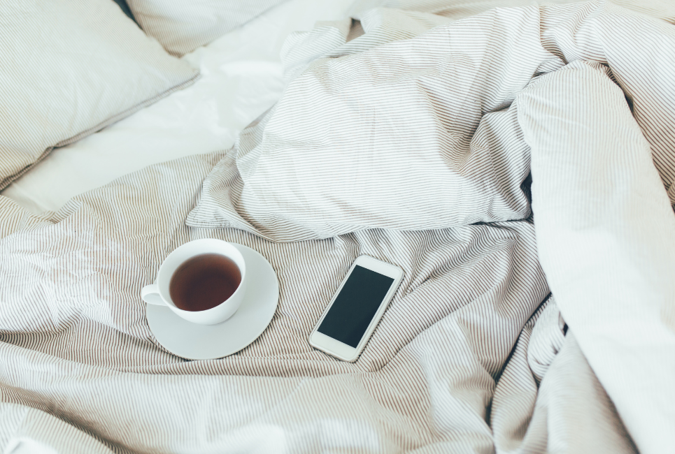 cream striped bedding with cup of tea and smartphone on bed