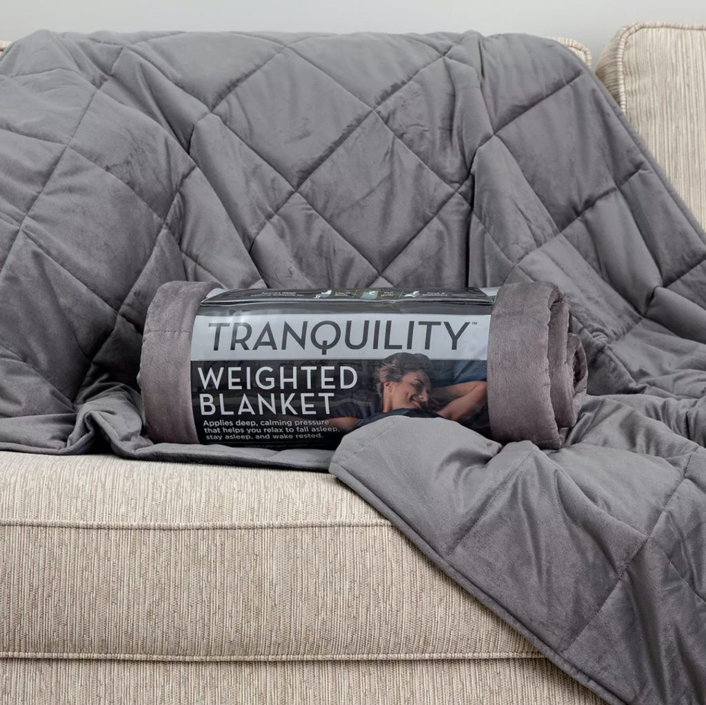 grey weighted blanket in package on couch with blanket draped over
