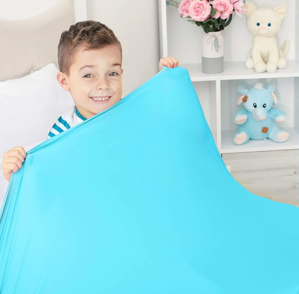 little boy holding up bright blue compression blanket over him