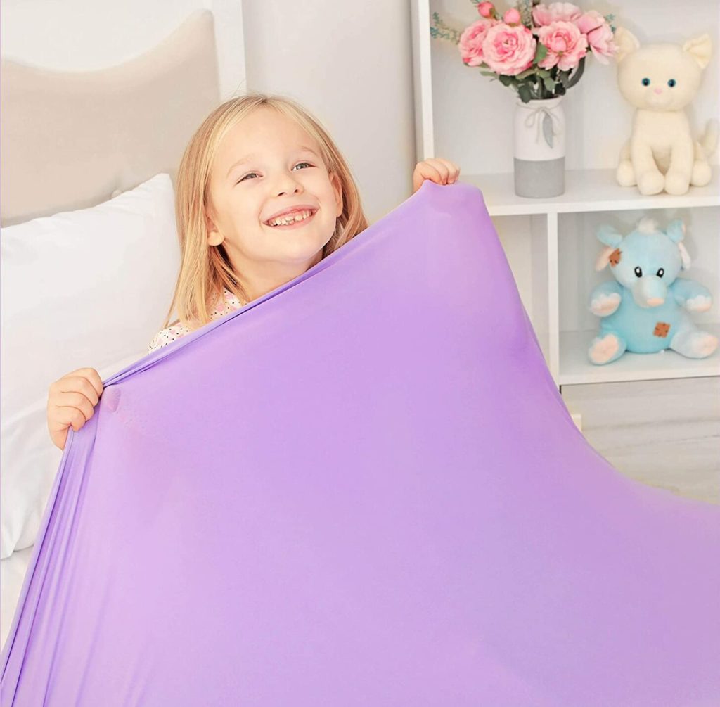 little girl holding up purple compression blanket over him