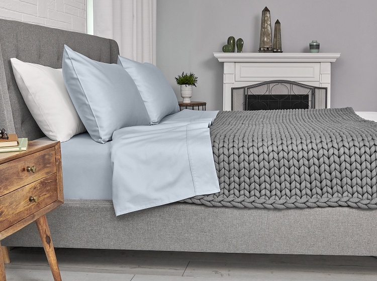 neatly made bed shown from side with light blue sheets and grey knitted weighted blanket