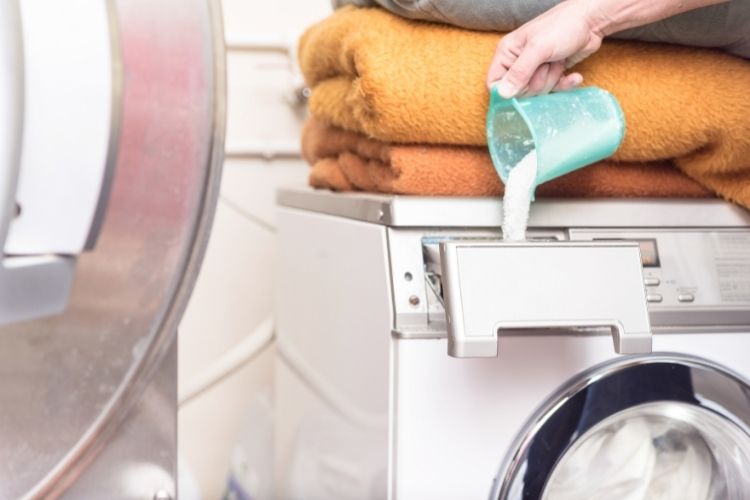persons hand pouring detergent into laundry dispenser