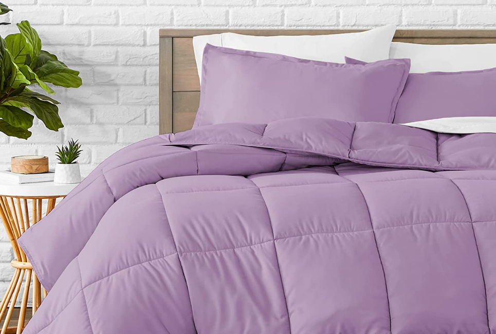 purple box stitch comforter on bed with white brick wall behind bed