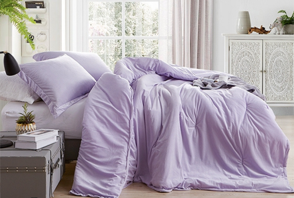 unmade bed with lavender comforter shown from side