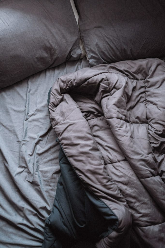 unmade bed with dark grey bedding