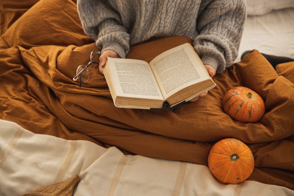 woman reading book in bed with pumpkins on orange comforter