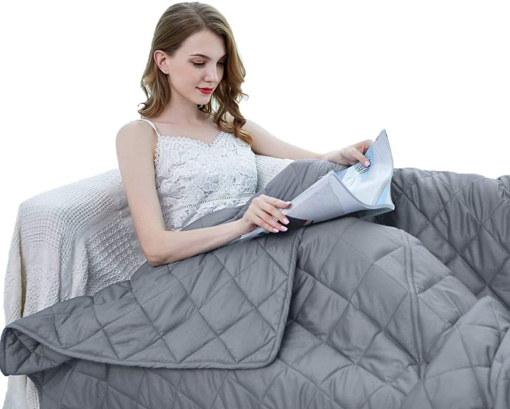woman sitting up reading book with grey blanket over her
