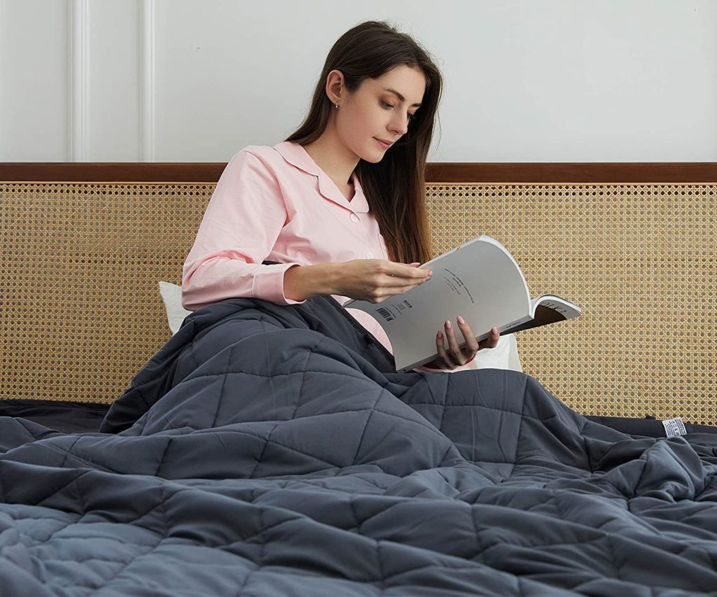 woman sitting up reading in bed under grey weighted blanket