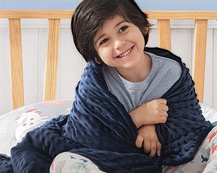 young child sitting up smiling with blue blanket wrapped around him